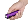 Mano sosteniendo una linterna LED Olight morada compacta y texturizada contra fondo blanco