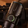 Linterna Olight Warrior 3S negra con indicador de batería LED, sobre superficie de rifle texturizada.