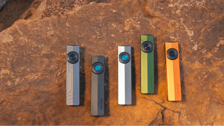Cinco linternas Olight de colores (gris, verde, naranja) sobre roca marrón.