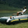 Bote inflable Intex verde en la orilla del lago con mini bomba de aire naranja y hombre relajándose al fondo